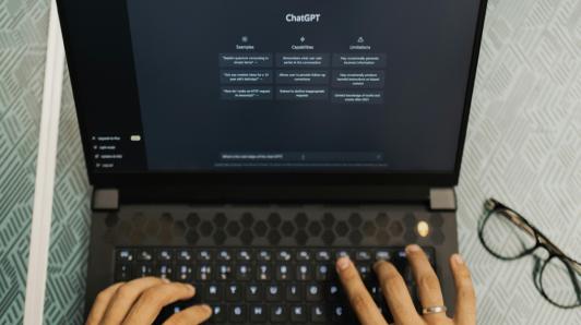 First person view of a woman typing a question into ChatGPT on her laptop.