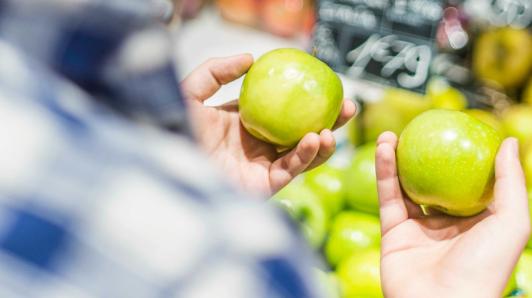 Close up of a man holding a green apple in each hand, trying to decide between them.